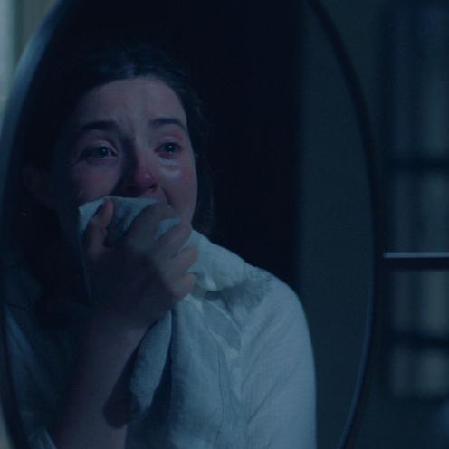 Nærbillede af en grædende kvinde, der dækker munden med et stykke stof.